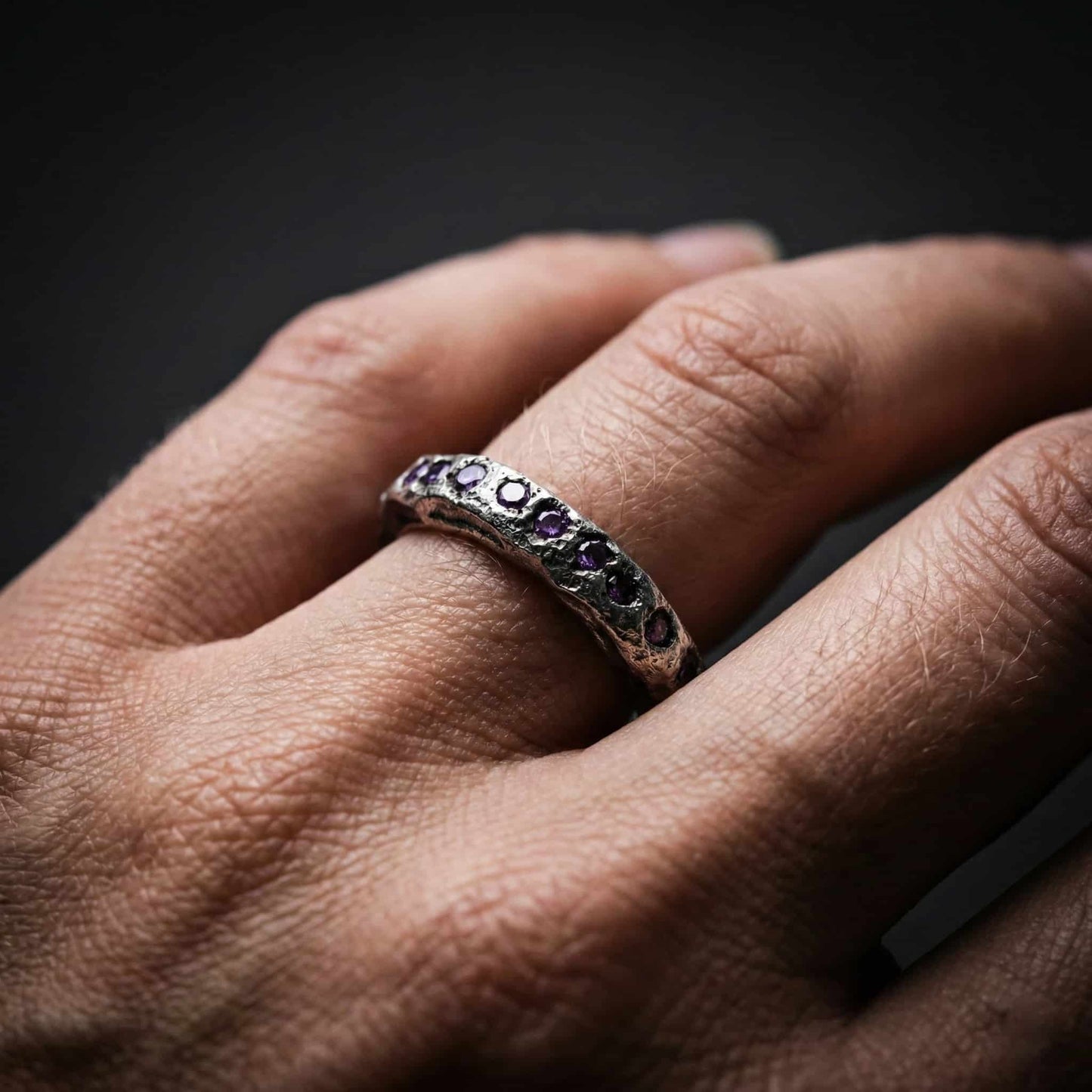 Anillo sin fin modelo Eternity de plata con piedras tono amatista en mano de mujer.