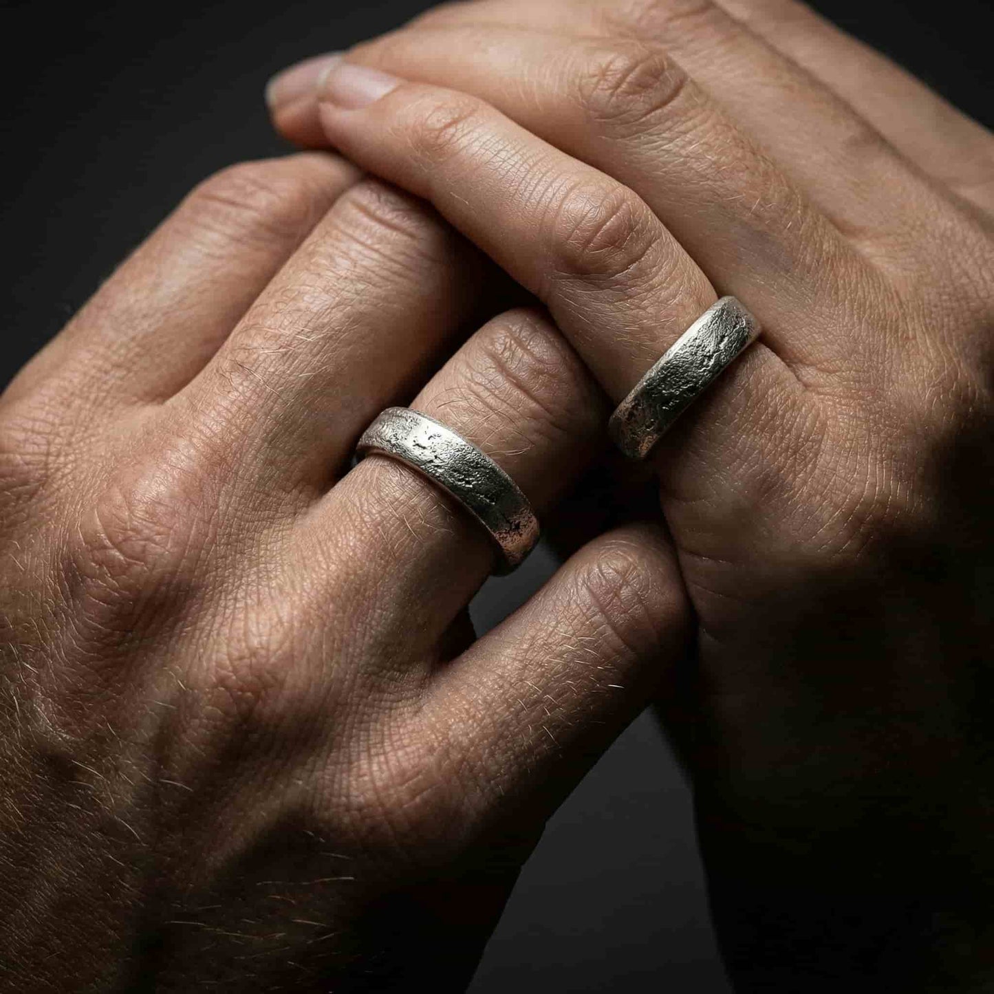 Detalle de manos de novios con alianzas artesanales modelo Duna textura arena.