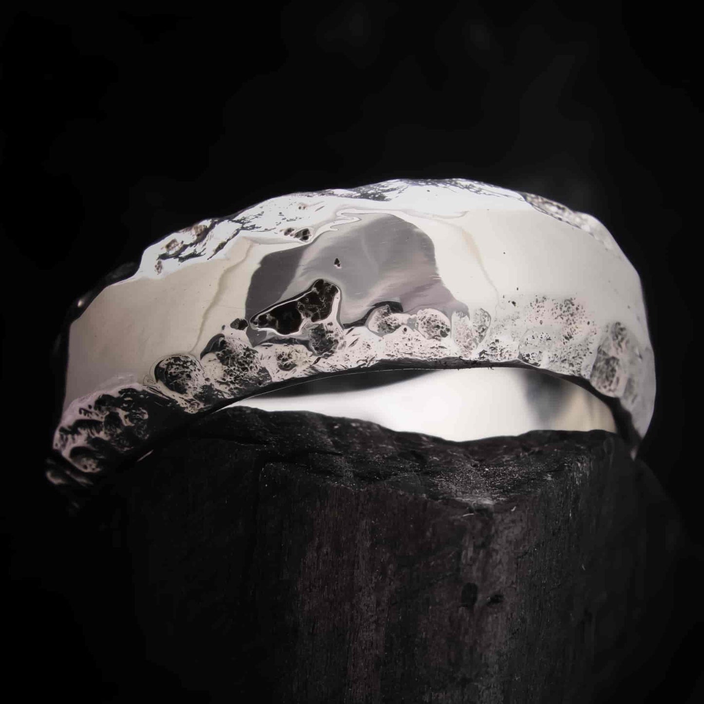 Anillo de boda plateado con acabado pulido brillante y fondo rugoso oscuro.