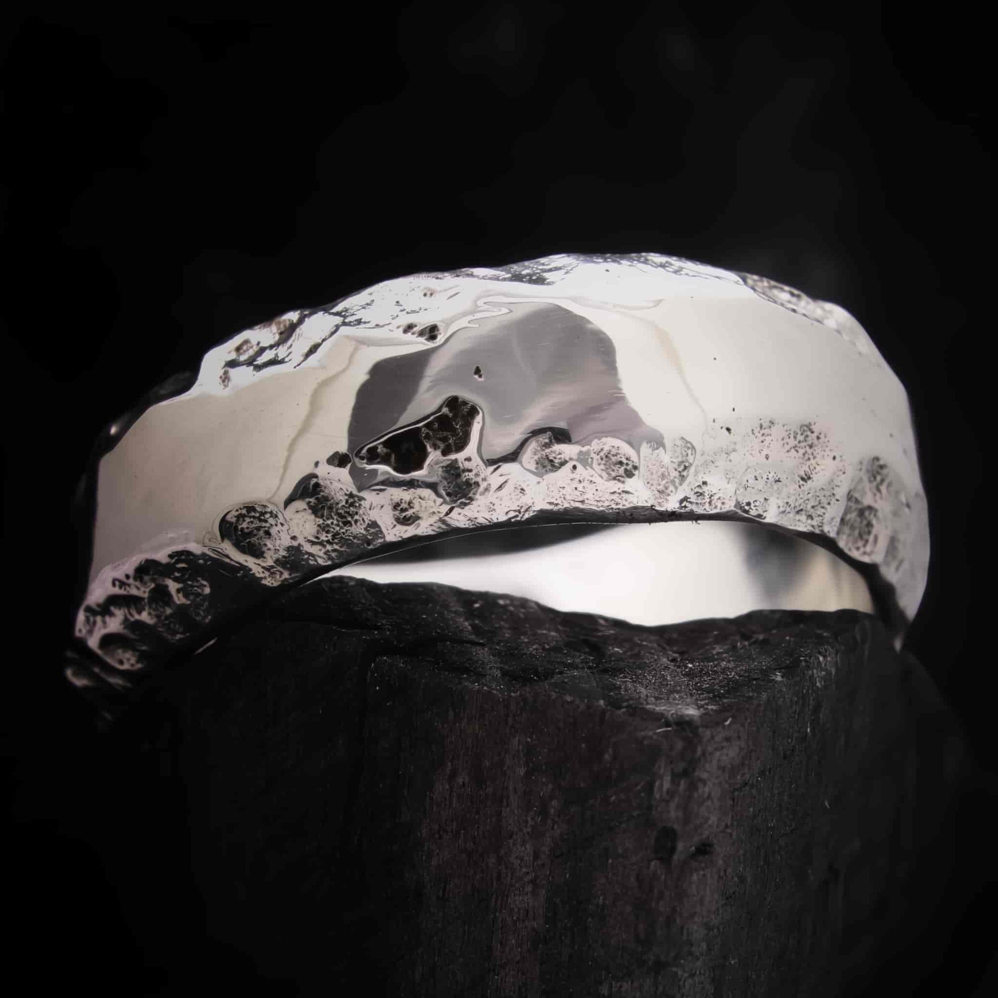 Anillo de boda plateado con acabado pulido brillante y fondo rugoso oscuro.