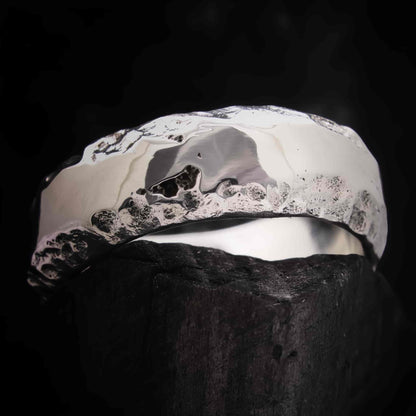 Anillo de boda plateado con acabado pulido brillante y fondo rugoso oscuro.