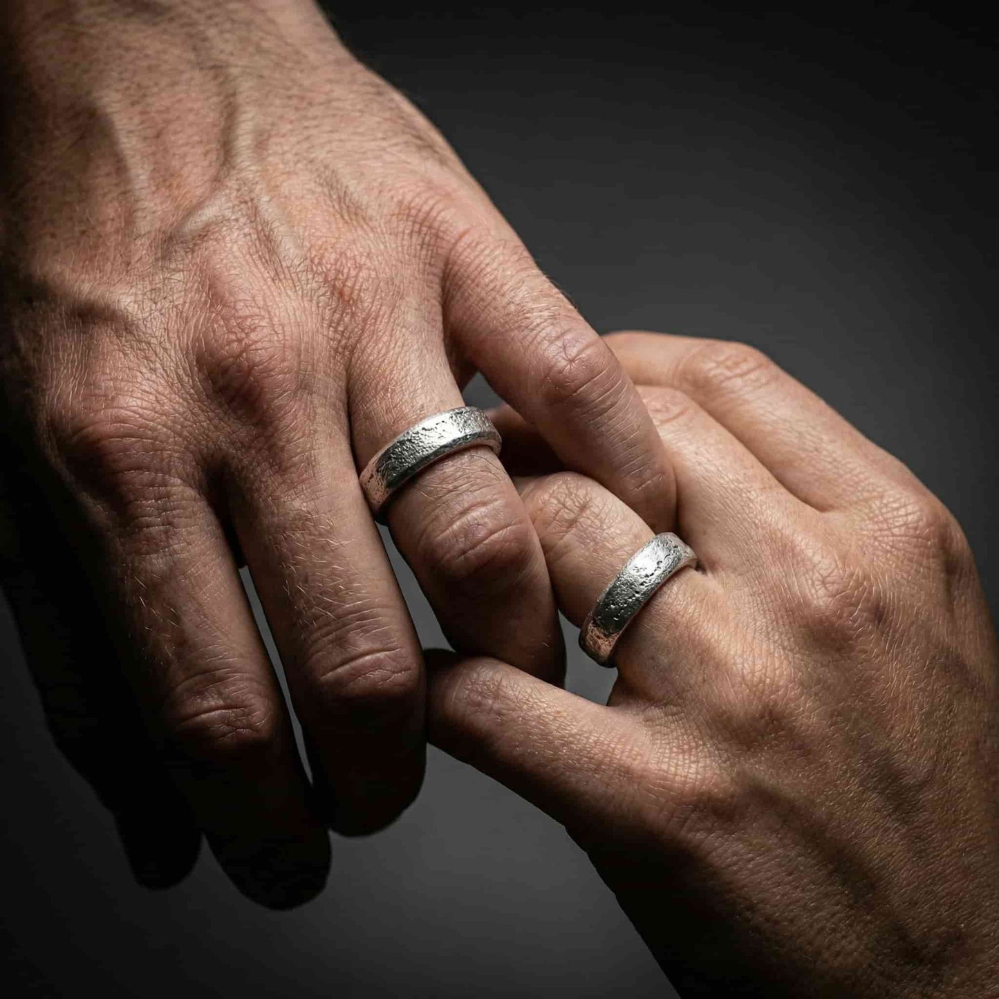 Alianza ancha para hombre puesta en la mano con acabado brillante texturizado.