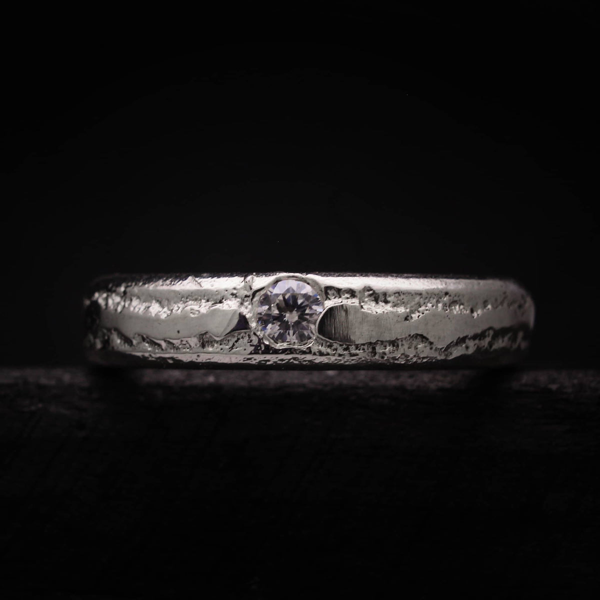 Alianza artesanal de plata maciza con circonita central y textura rústica orgánica.
