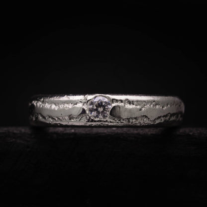 Alianza artesanal de plata maciza con circonita central y textura rústica orgánica.