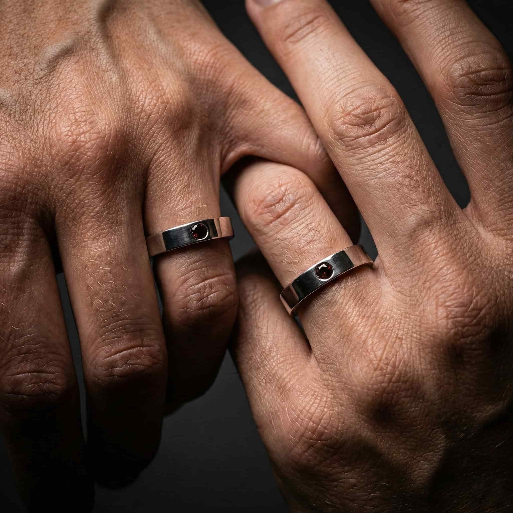 Alianza de boda de plata lisa con granate natural puesta en mano de mujer y hombre.
