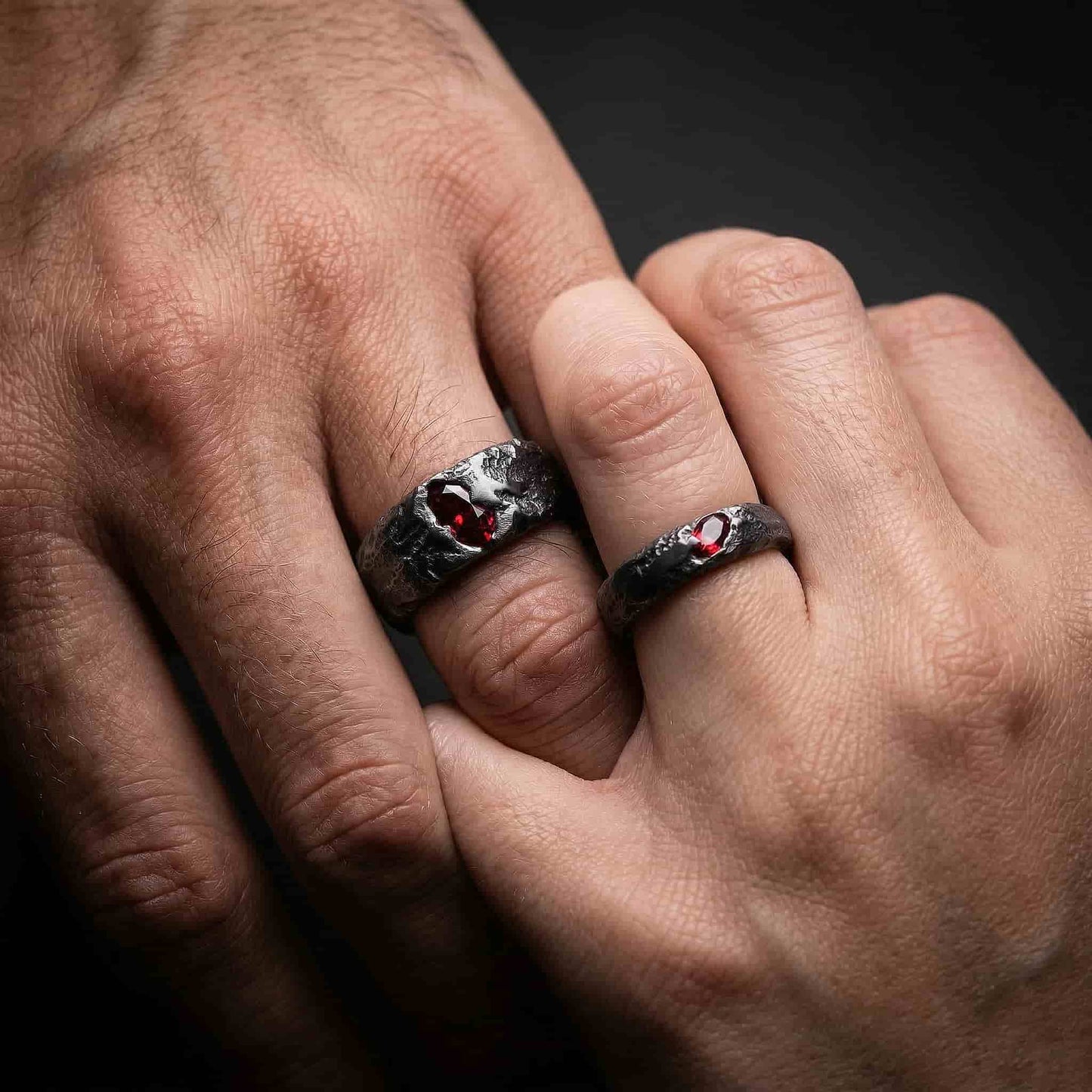 Un set de dos alianzas de boda de plata negra forjada con circonitas rojas, de estilo gótico e industrial.