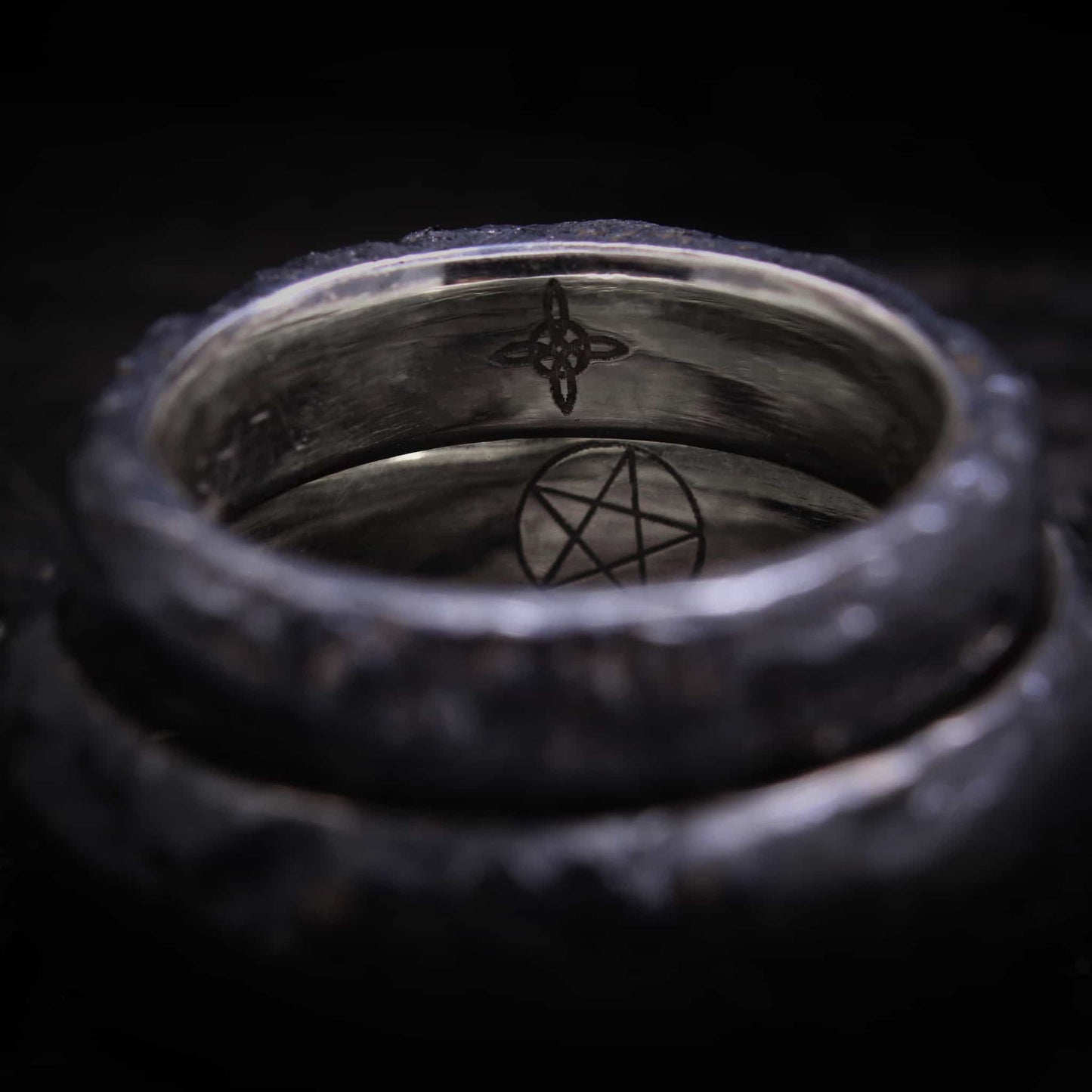 Vista lateral de dos anillos de boda texturizados de plata negra con circonitas rojas ovaladas apilados sobre una superficie oscura.