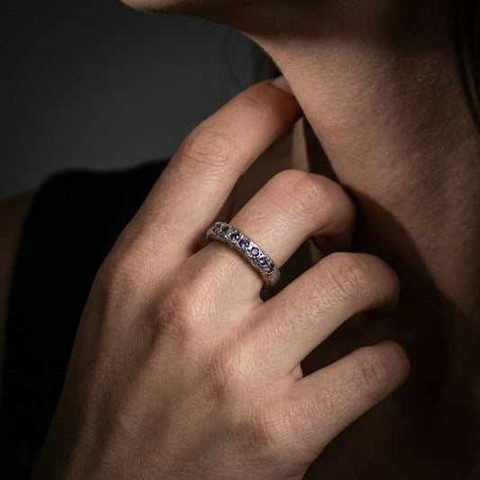 Anillo eternidad de plata brillante con diseño irregular y circonitas moradas incrustadas.