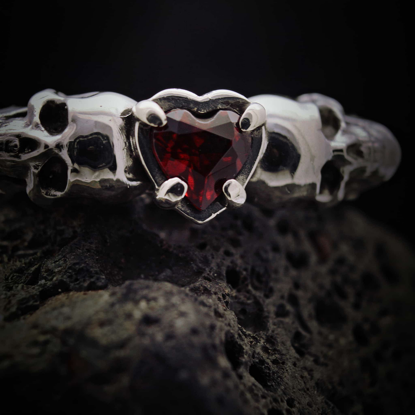 Detalle de anillo gótico de plata de ley 925 con acabado envejecido y piedra roja intensa.