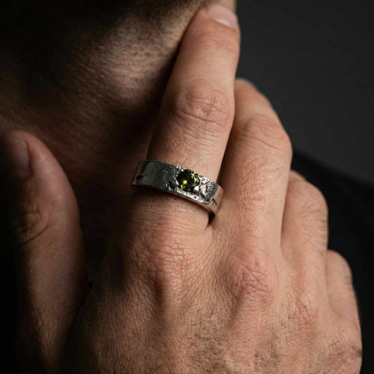 Primer plano de mano masculina con anillo de plata ancho de 6mm puesto en el dedo. Se aprecia la textura rústica y la piedra verde.