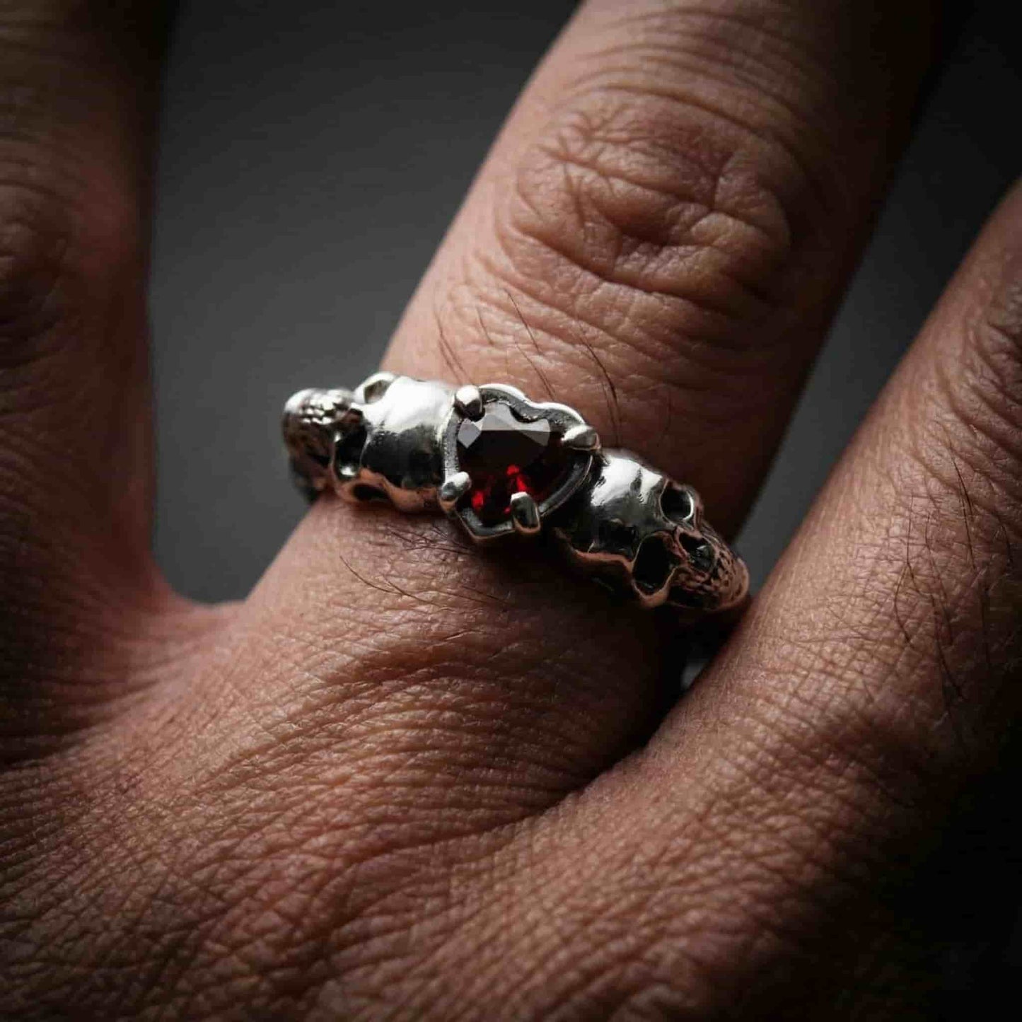 Anillo de plata para hombre con diseño de calaveras y piedra granate en forma de corazón.