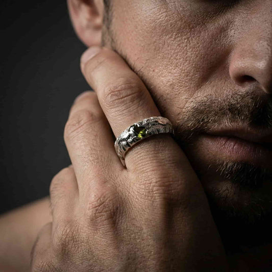 Hombre luciendo un anillo artesanal de plata con piedra verde peridoto en la mano.