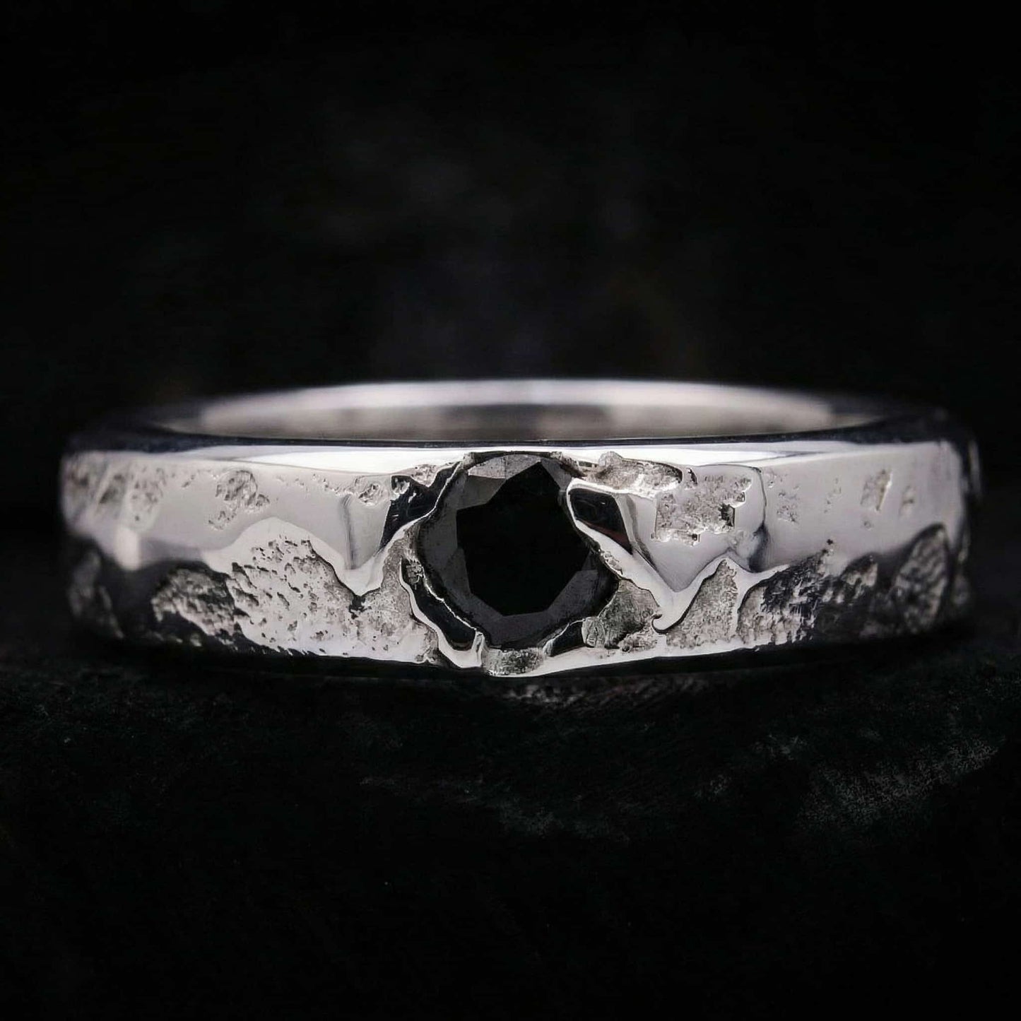 Primer plano del anillo de plata artesanal para hombre mostrando su textura rústica y la circonita negra central.