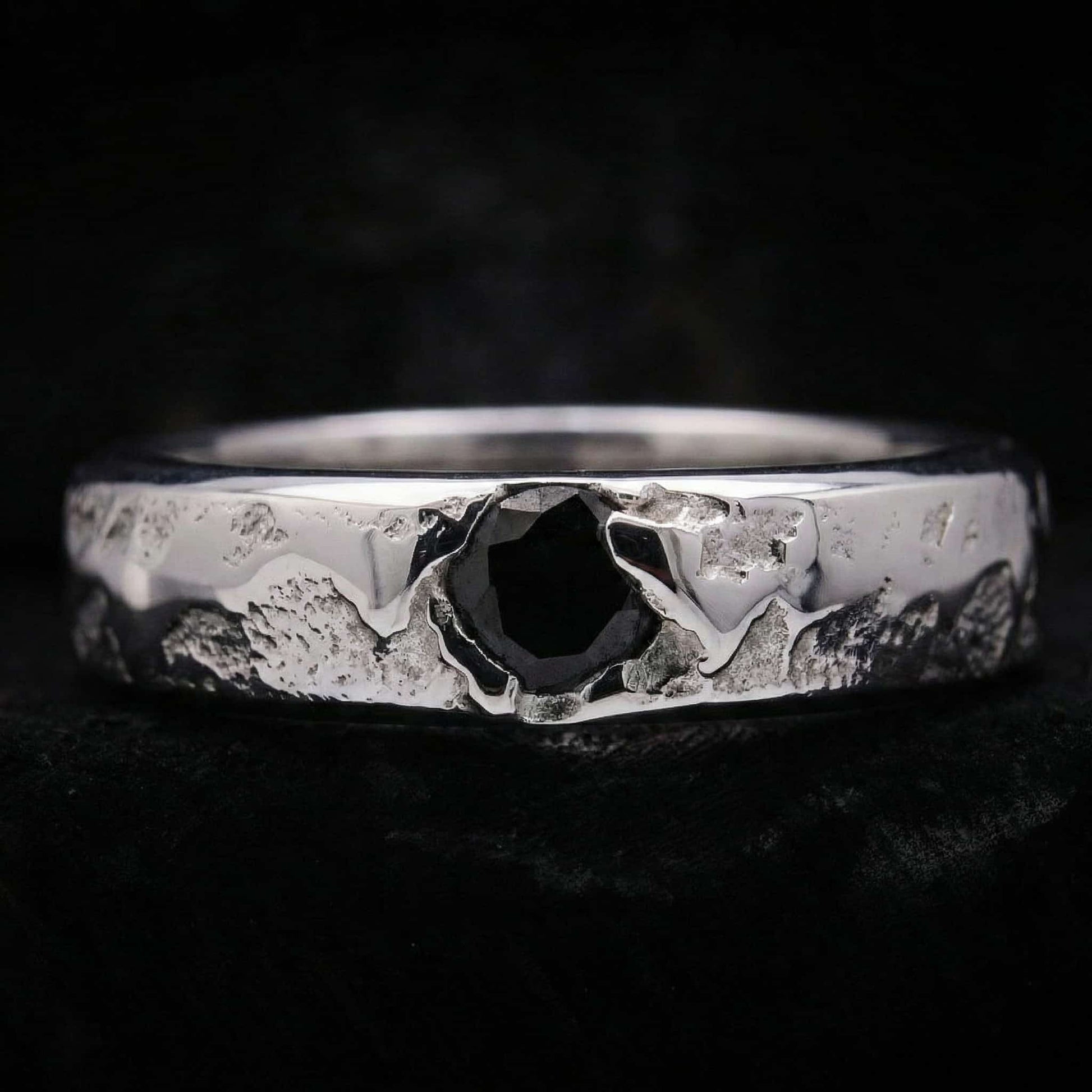 Primer plano del anillo de plata artesanal para hombre mostrando su textura rústica y la circonita negra central.