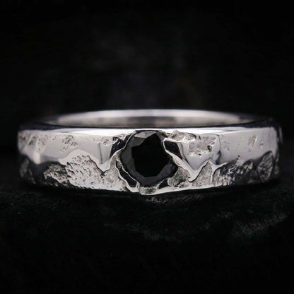 Primer plano del anillo de plata artesanal para hombre mostrando su textura rústica y la circonita negra central.