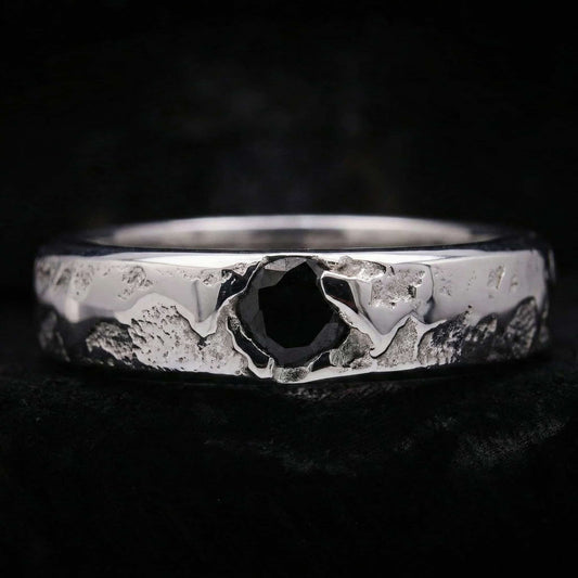 Primer plano del anillo de plata artesanal para hombre mostrando su textura rústica y la circonita negra central.