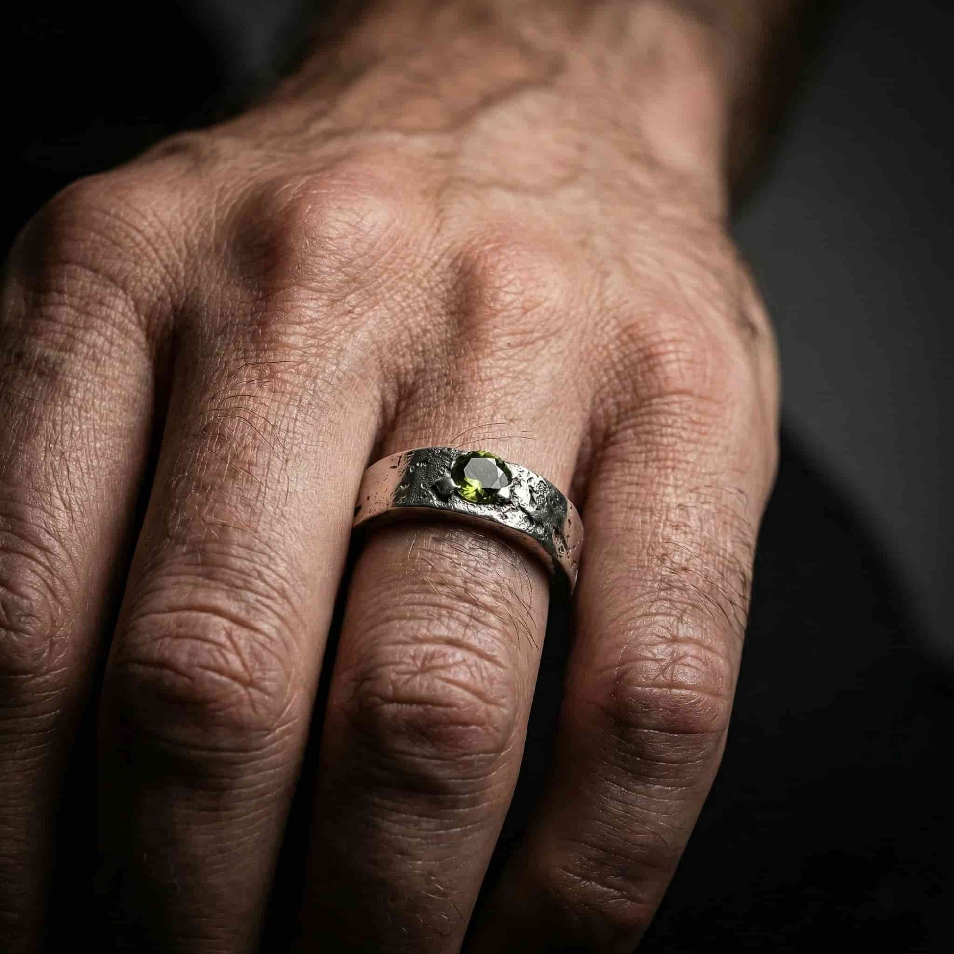 ​Modelo masculino luciendo un anillo de sello artesanal en plata con peridoto. Joyería de hombre estilo dark y alternativo.