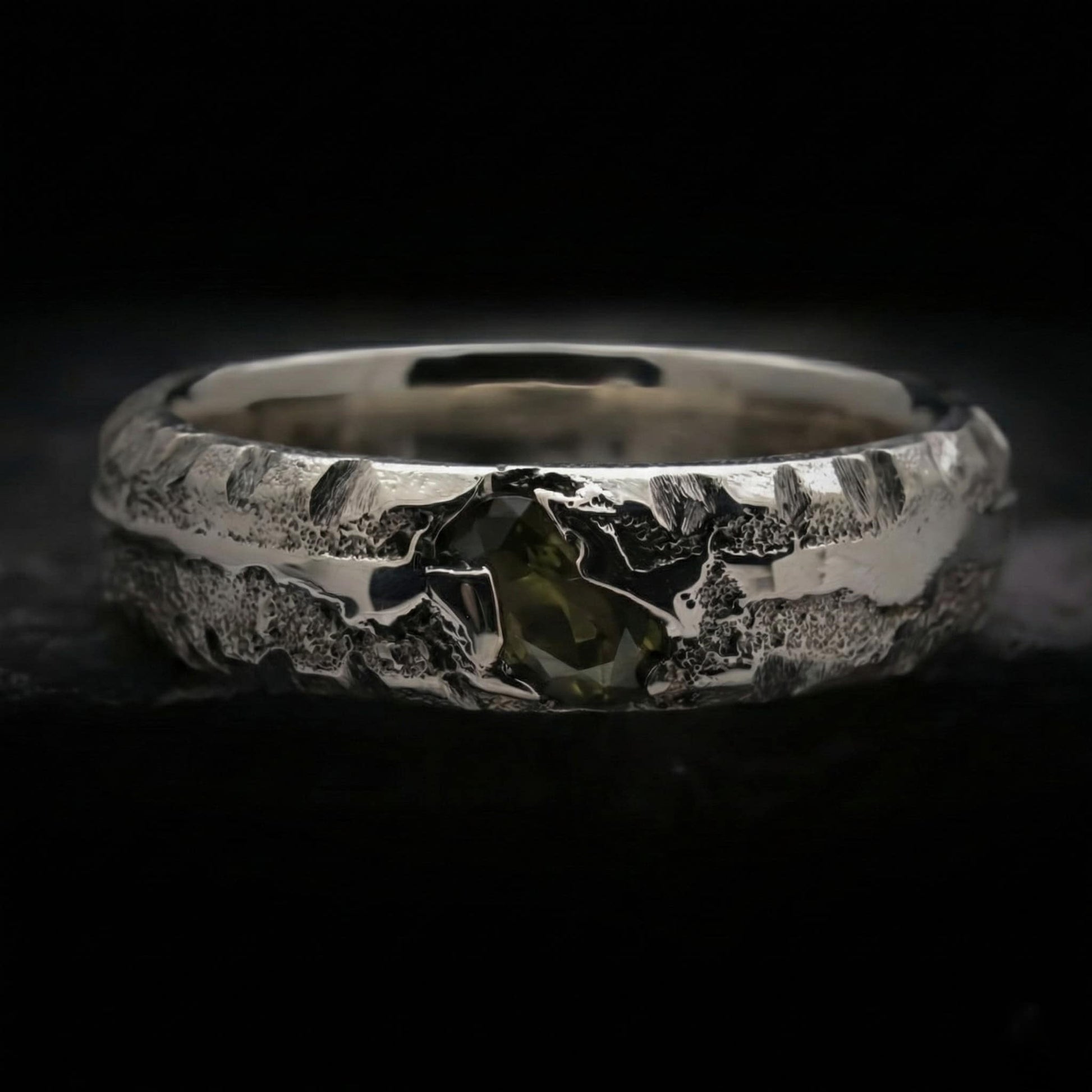 Detalle de anillo para hombre con circonita verde peridoto de plata con textura rústica.