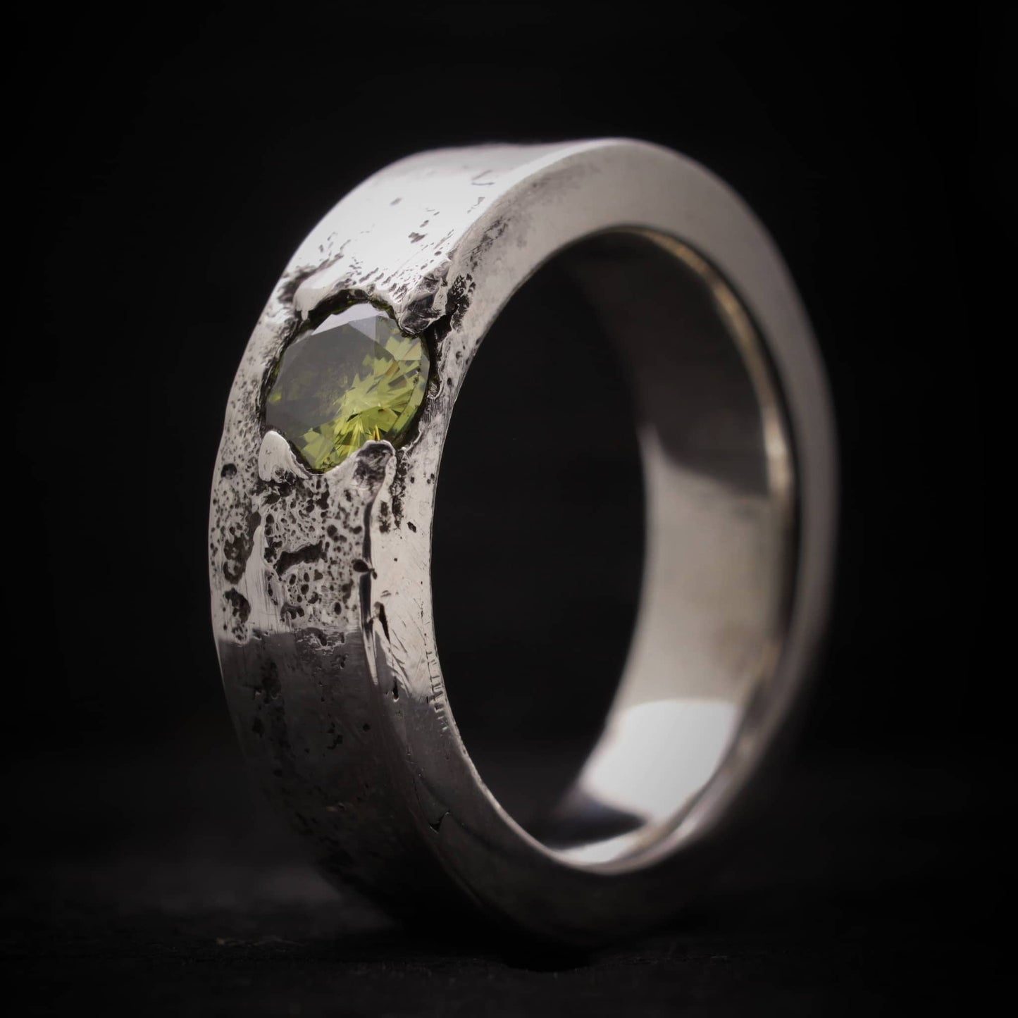 Primer plano de la textura orgánica y el engaste de la piedra peridoto en anillo de plata ancho.