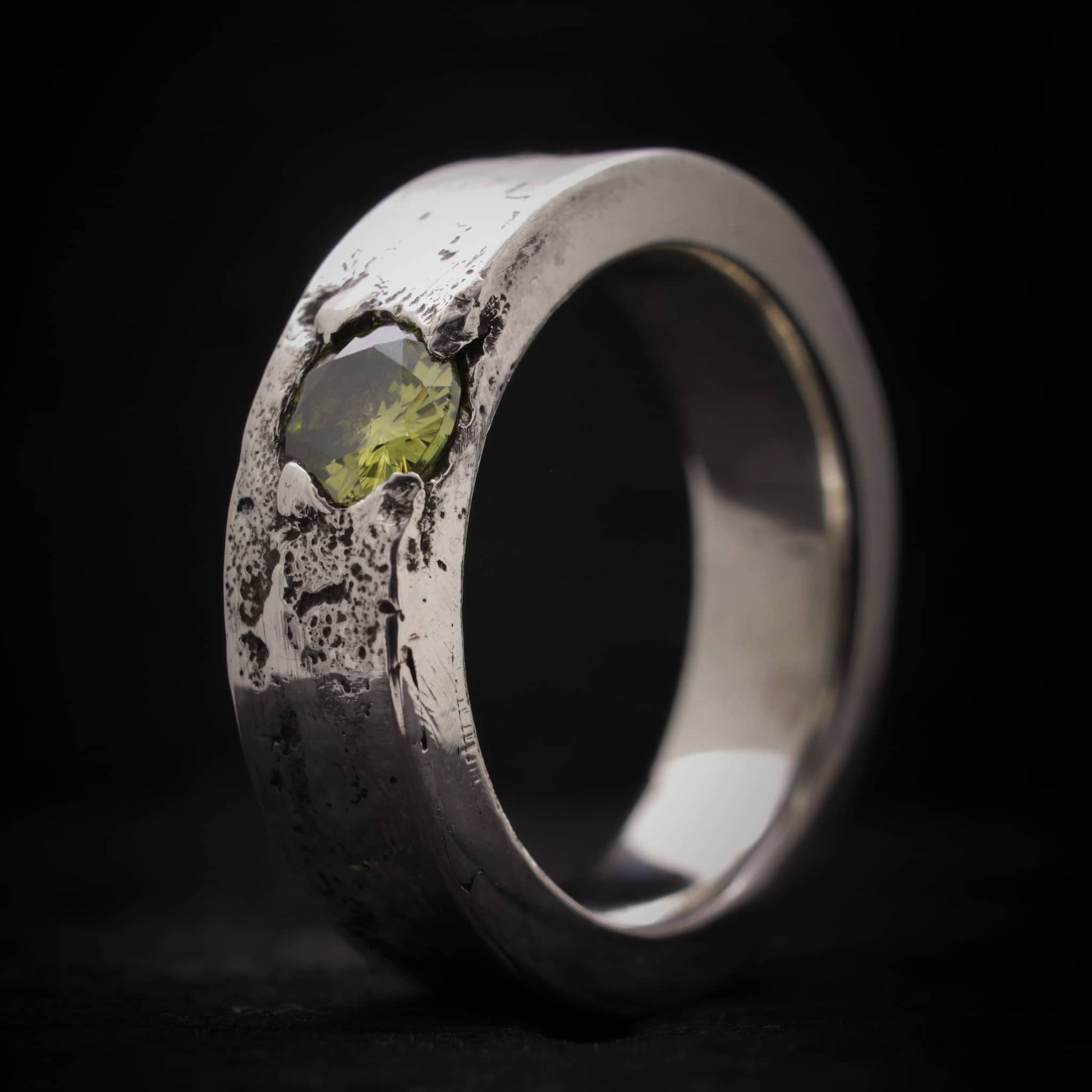 Primer plano de la textura orgánica y el engaste de la piedra peridoto en anillo de plata ancho.