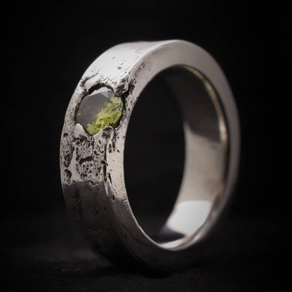 Primer plano de la textura orgánica y el engaste de la piedra peridoto en anillo de plata ancho.