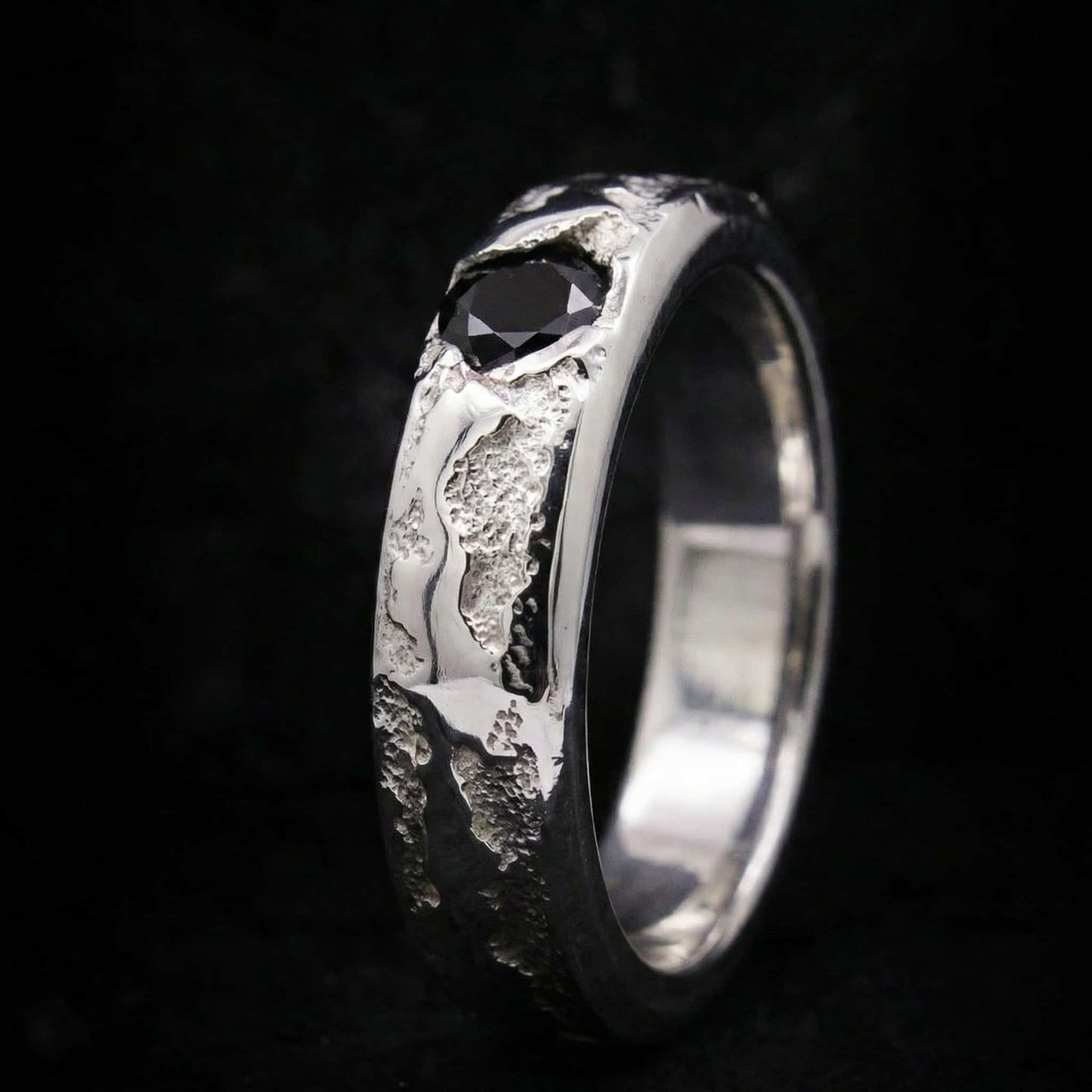 Vista lateral de anillo tipo sello de plata maciza con acabado texturizado y piedra negra incrustada.