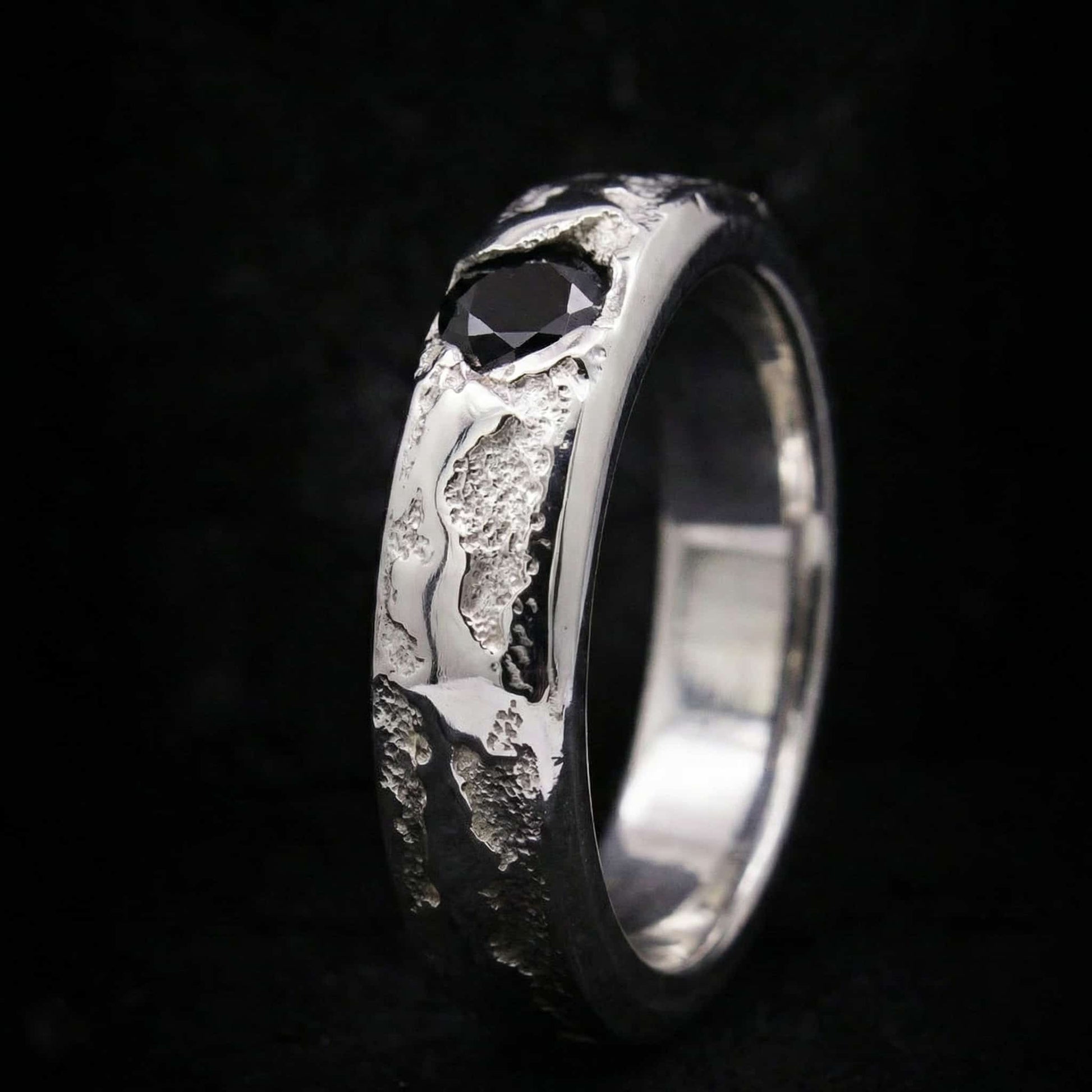 Vista lateral de anillo tipo sello de plata maciza con acabado texturizado y piedra negra incrustada.