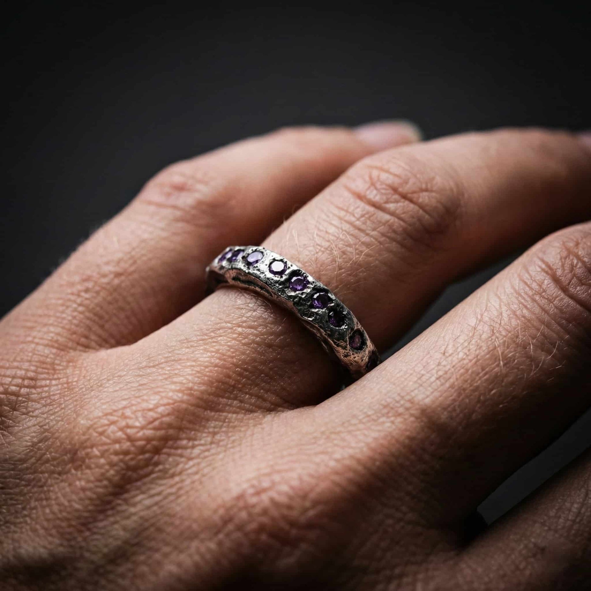Anillo sin fin modelo Eternity de plata con piedras tono amatista en mano de mujer.