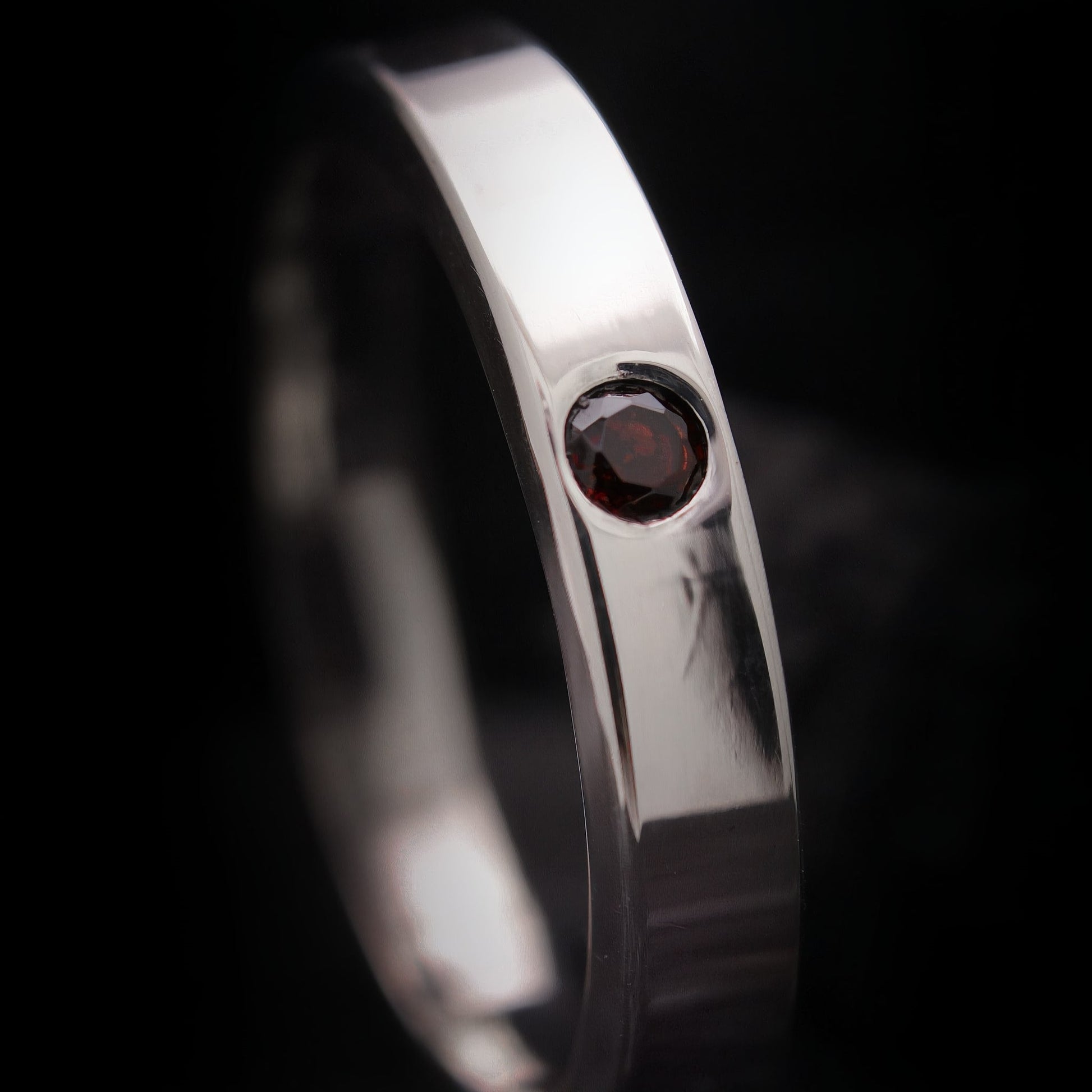 Detalle de granate natural rojo engastado en anillo de plata pulida.