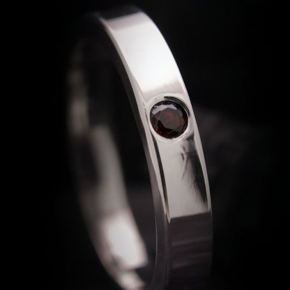 Detalle de granate natural rojo engastado en anillo de plata pulida.