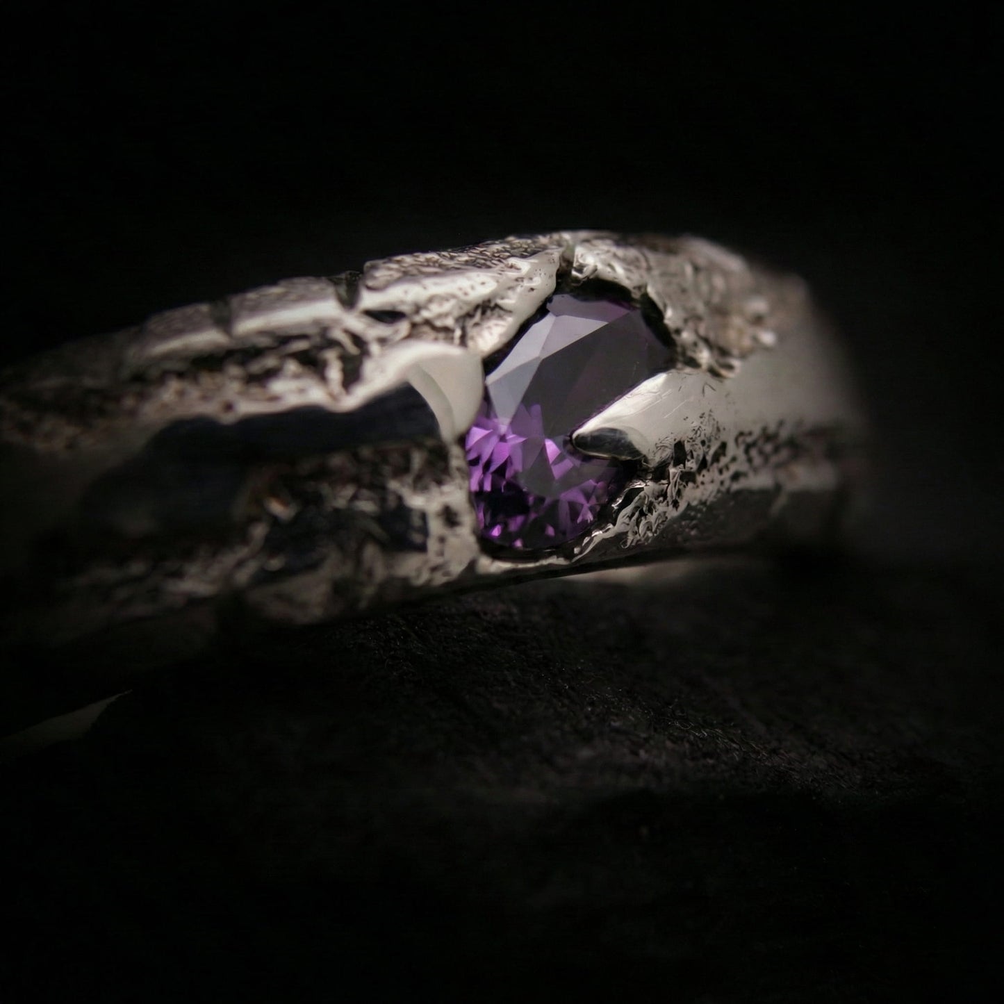 Primer plano de la textura porosa del anillo de plata forjado en arena con piedra.