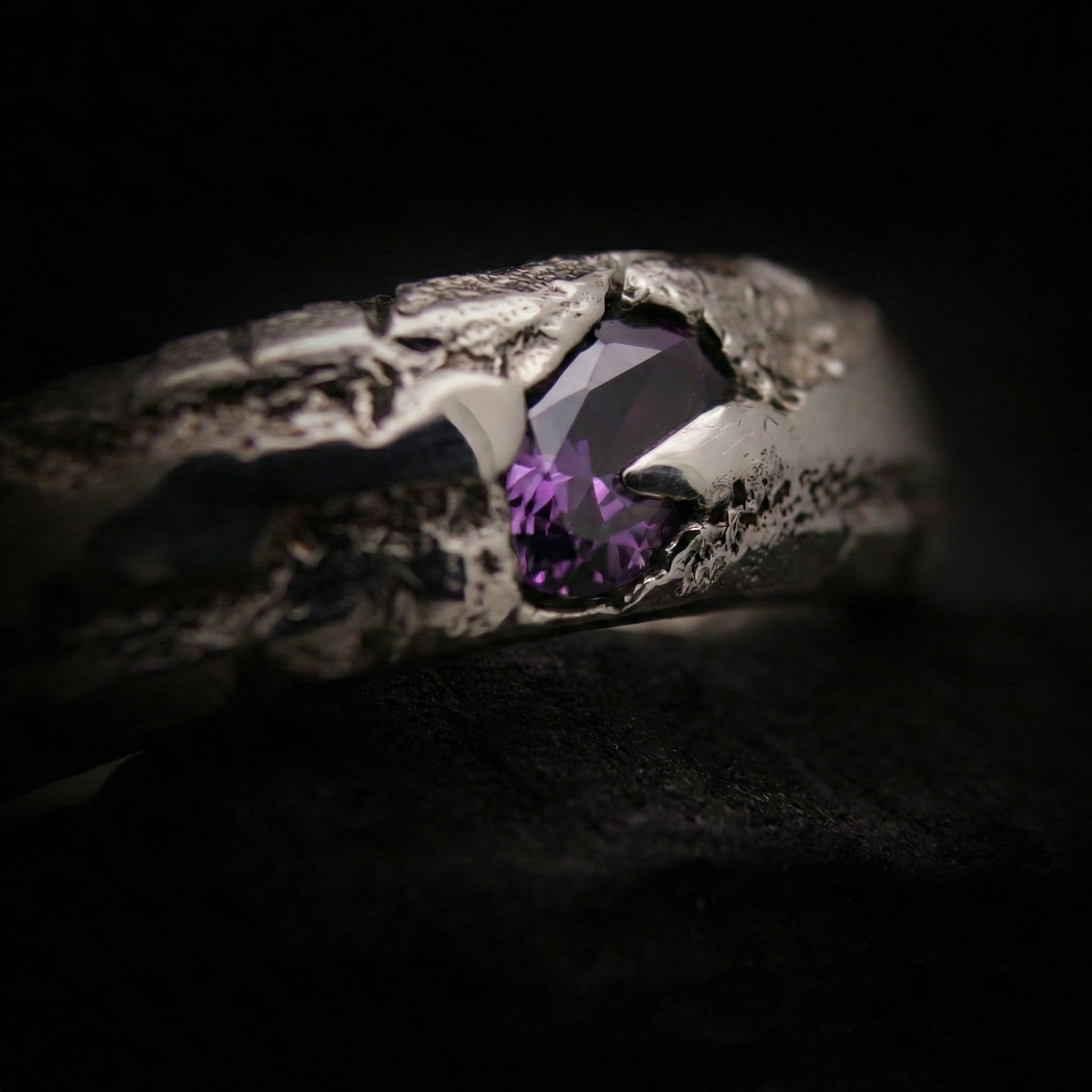 Primer plano de la textura porosa del anillo de plata forjado en arena con piedra.