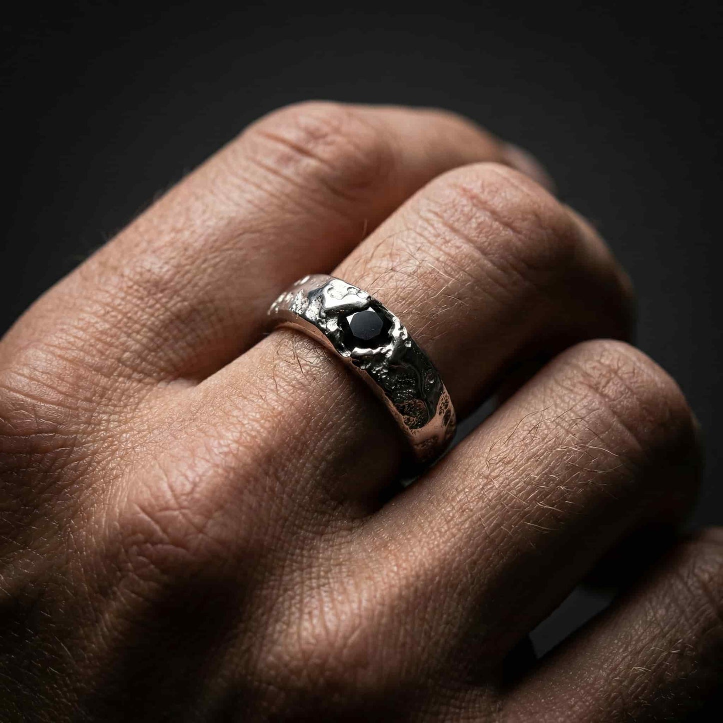 Primer plano de mano masculina luciendo el anillo de plata robusta y piedra negra, estilo auténtico.
