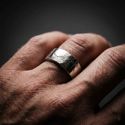Primer plano de anillo statement grueso de plata en mano masculina, destacando el estilo brutalista.