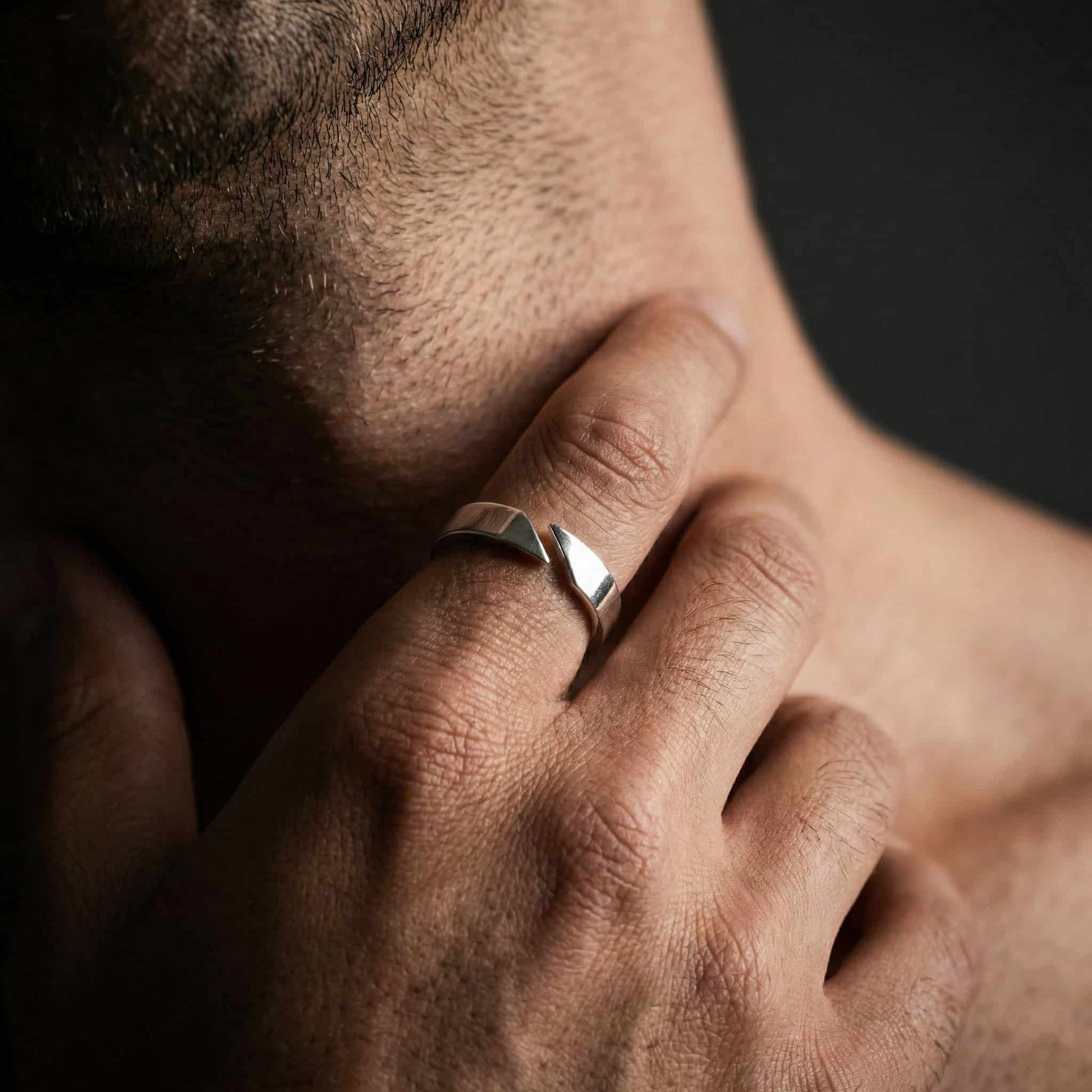 Primer plano de mano masculina con anillo abierto de plata y diseño geométrico moderno.