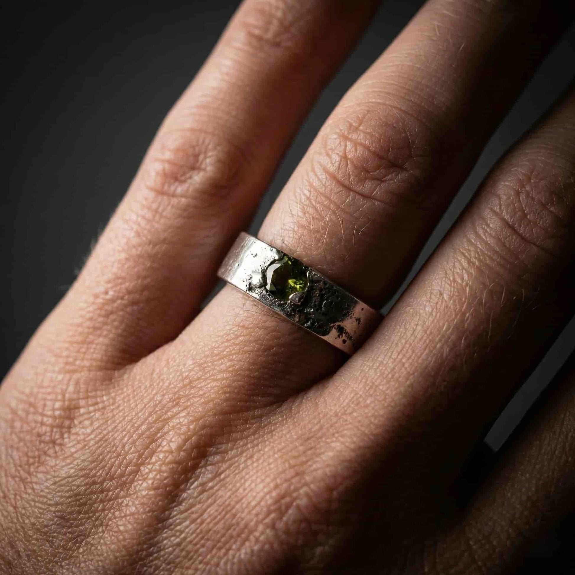 Primer plano de una mano con el anillo Legado de plata, mostrando el detalle de las cenizas y el brillo de la circonita peridoto.