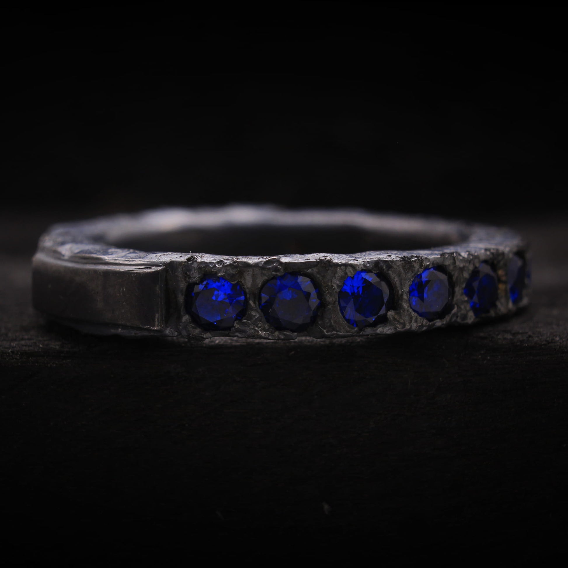 Detalle de la textura oxidada y piedras azules en anillo de estilo brutalista para hombre.